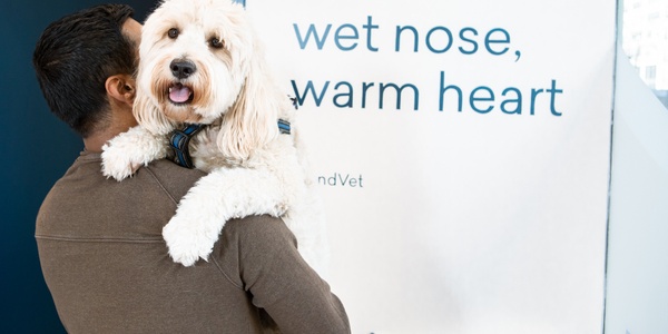 A person holding a fluffy white dog near a sign that reads "wet nose, warm heart.