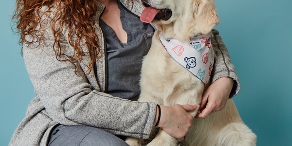 A woman smiling at her happy golden retriever wearing a bandana.